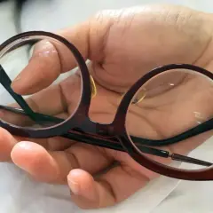 Okrągłe okulary w brązowej oprawce, idealne okulary dla pracownika, trzymane w dłoni.