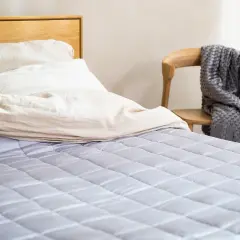 Łóżko z jasną pościelą i szarą kołdrą obok. Dowiedz się, jakie kołdry są najzdrowsze dla Twojego snu.