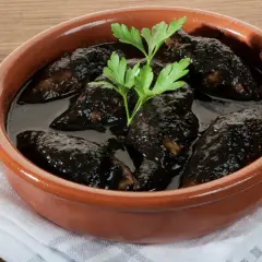 Chipirones en salsa negra, un plato tradicional servido en cazuela de barro, con perejil fresco y un tenedor al lado.