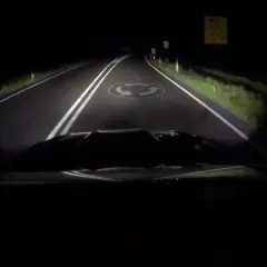 La route de nuit, éclairée par les feux de route, révèle un rond-point.
