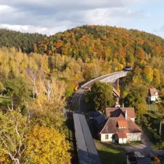 Jesienny krajobraz Gór Sowich. Kolorowe lasy otaczają tory kolejowe i most.