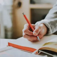 Hand schreibt in ein Notizbuch. Die Person überlegt vielleicht, wie sie ihren **Dolmetscher Gehalt** optimieren kann.