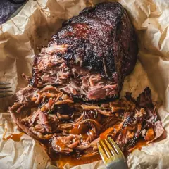 Saftiges pulled pork, zart zerfallen, mit BBQ-Sauce übergossen, auf Backpapier mit Gabeln.
