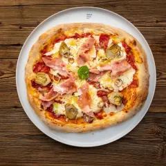 Eine köstliche Pizza mit Prosciutto Crudo, Artischocken und frischem Basilikum auf einem weißen Teller, serviert auf rustikalem Holz.