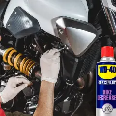Hombre con guantes blancos trabajando en la cadena de moto. Lata de WD-40 Specialist Bike Degreaser para quitar oxido cadena moto.