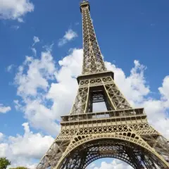 Vue en contre-plongée du برج ايفل sous un ciel bleu parsemé de nuages blancs.