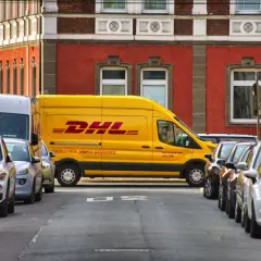 Żółta furgonetka DHL zaparkowana na ulicy, obok inne samochody. Może być potrzebny protokół szkody.