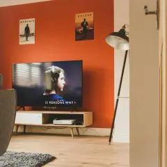 Pomarańczowe ściany świetnie komponują się z szarością kanapy i dywanu. W salonie wisi plakat z filmu "Driver".