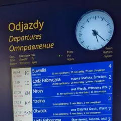 Tablica odjazdów pociągów z informacją o opóźnieniach, wskazująca na utrudnienia w ruchu pociągów. Zegar pokazuje aktualny czas.