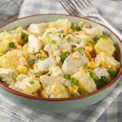 Insalata di pollo e patate cremosa con mais, uova sode e cipollotto fresco, servita in una ciotola verde.