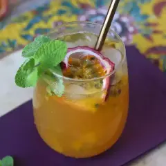 Un délicieux cocktail thé glacé aux fruits de la passion, garni de menthe fraîche et d'une tranche de fruit.