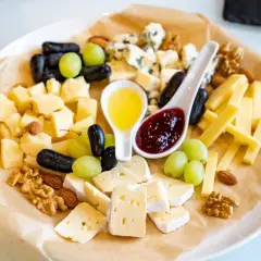 Tagliere di formaggi misti con uva, noci, mandorle e due cucchiaini: uno con miele dorato, l'altro con una deliziosa marmellata per formaggi.