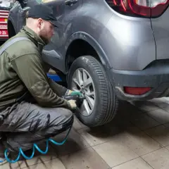 Mechanik w warsztacie dokonuje zmiany opon na zimowe, używając klucza pneumatycznego do odkręcenia śrub w kole samochodu.