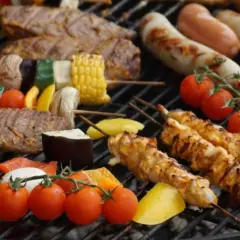 Na ruszcie grilluje się zdrowy grill: szaszłyki z kurczaka, wołowiny i warzyw, kiełbaski, pomidorki i kukurydza.