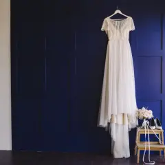 Elegancka suknia ślubna wisi na wieszaku, obok bukiet i buty. To inspiracja, jak przechowywać suknię ślubną, by zachowała swój blask.