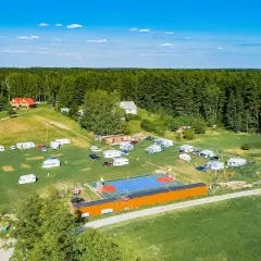 Nowy harsz: kemping z przyczepami, domkami i boiskiem sportowym otoczony lasem.