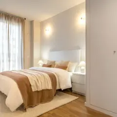 Dormitorio acogedor con cama vestida, cortinas vaporosas y apliques de pared que crean una atmósfera de luz cálida, neutra y fría.