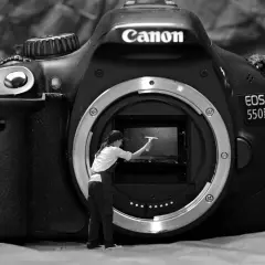 Miniaturowa postać czyści wnętrze aparatu Canon EOS 550D, pokazując, jak wyczyścić matrycę w aparacie.