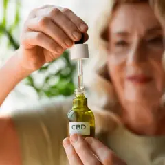 Kobieta trzyma buteleczkę olejku CBD. Zastanawia się, olejek CBD na co może jej pomóc w codziennym życiu.