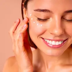 Une femme applique de la crème autour de ses yeux, un geste doux pour un massage des yeux relaxant.