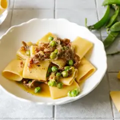 Piatto di paccheri conditi con piselli freschi e pezzetti croccanti di prosciutto crudo, un classico saporito.