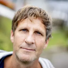 En snygg dansk skådespelare med blont, rufsigt hår och blå ögon ler mot kameran utomhus.
