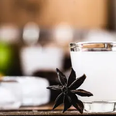 Mętny arak w szklance, obok gwiazdka anyżu, kostki lodu i zielona limonka.