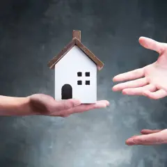 Manos intercambian una casa de juguete, simbolizando el reparto entre herederos.