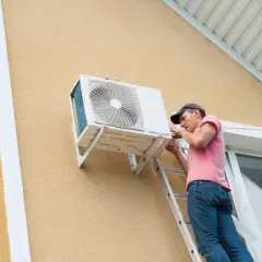 Técnico en escalera realizando la **instalación aire acondicionado exterior** en la pared de una casa.