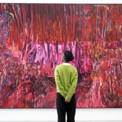 A person in a green sweater contemplates a vibrant, abstract painting, a visual guide on how to find up and coming artists.