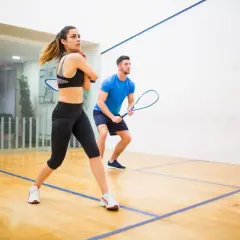 Para ćwiczy squasha, poznając zasady gry. Kobieta w sportowym stroju i mężczyzna w niebieskiej koszulce z rakietami gotowi do akcji na boisku.