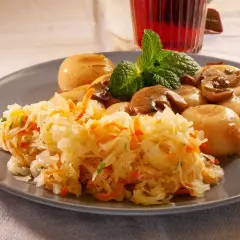 Pyszna sałatka z kiszonej kapusty z marchewką, podana z duszonymi pieczarkami i kluskami, ozdobiona miętą.