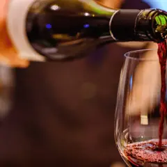 Czerwone wino leje się z butelki do kieliszka, tworząc piankę. Widać bogactwo **tannin w winie**, które nadają mu głębię.