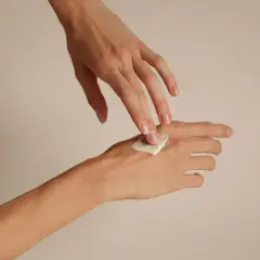 Dłonie nakładające krem na skórę, pokazujące naturalne paznokcie.