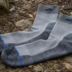 Gray hiking socks with blue mountain logos lie on the forest floor. Learn how to choose hiking socks for comfort and support.