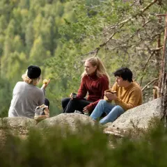 Vänner fikar på en klippa vid STF Undersvik med skogen som bakgrund.