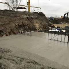 Budowa w toku: świeża wylewka betonowa na zewnątrz, zbrojenie i koparki w tle.