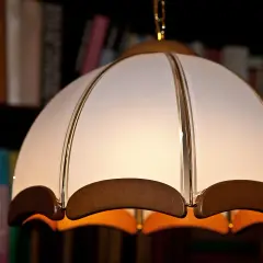 Jak wyczyścić abażur z materiału? Delikatne czyszczenie lampy wiszącej z białego materiału i drewna, na tle regału z książkami.