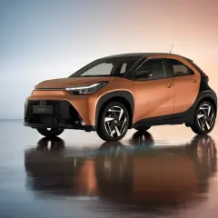 Pomarańczowy Toyota Aygo Cross z czarnymi akcentami i stylowymi felgami, odbijający się w lustrzanej podłodze.