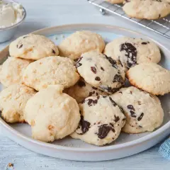 Leckere Cheesecake Cookies mit Schokoladenstückchen auf einem Teller, daneben eine Schüssel Frischkäse.