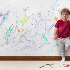 Chłopiec stoi przy ścianie pokrytej kolorowymi bazgrołami. Czy to oznaka, jak rozpoznać ADHD u dziecka?