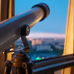 Teleskop na statywie skierowany na miasto o zachodzie słońca.