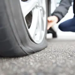 Une personne accroupie examine un pneu crevé, signe qu'il faut s'arrêter et changer la roue.
