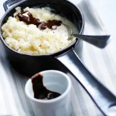 Un délicieux riz au lait au chocolat, servi dans une petite casserole noire, avec une cuillère et un ramequin de sauce chocolat.