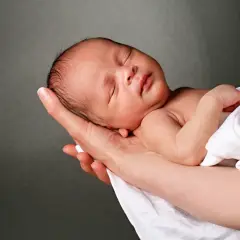 Słodki noworodek śpi w ramionach, otulony białym materiałem. To jak surogatka, która tuli swoje najcenniejsze skarby.