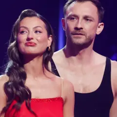 Kamil Nożyński i jego partnerka, w czerwonej sukni i czarnym topie, prezentują się na scenie.