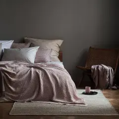 Gemütliches Schlafzimmer mit Bett in altrosa und grau, Korb-Sessel und Kerzenlicht.