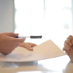 Dłonie trzymają dokumenty i długopis. Czy to umowa, czy może wpis do bazy nieuczciwych wynajmujących?