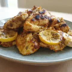En tallrik med saftig, grillad kallskuren kyckling med citronskivor. Kryddorna ger kycklingen en härlig färg.