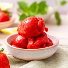 Schüssel mit leuchtend rotem Erdbeer-Sorbet, perfekt zum Sorbet selber machen. Frische Erdbeeren und Zitronenspalten im Hintergrund.